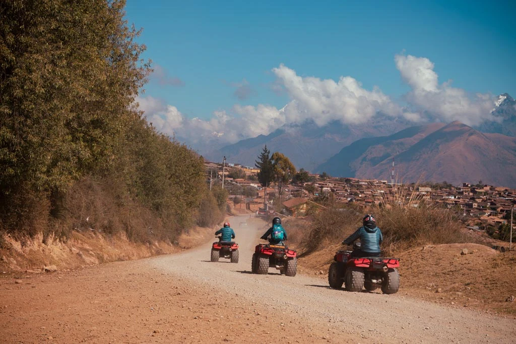 Tourists riding ATVs on a dirt road through the Maras town in Peru